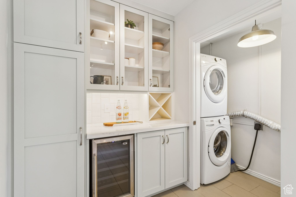 Laundry area with wine cooler, stacked washing machine and dryer, and a dry bar