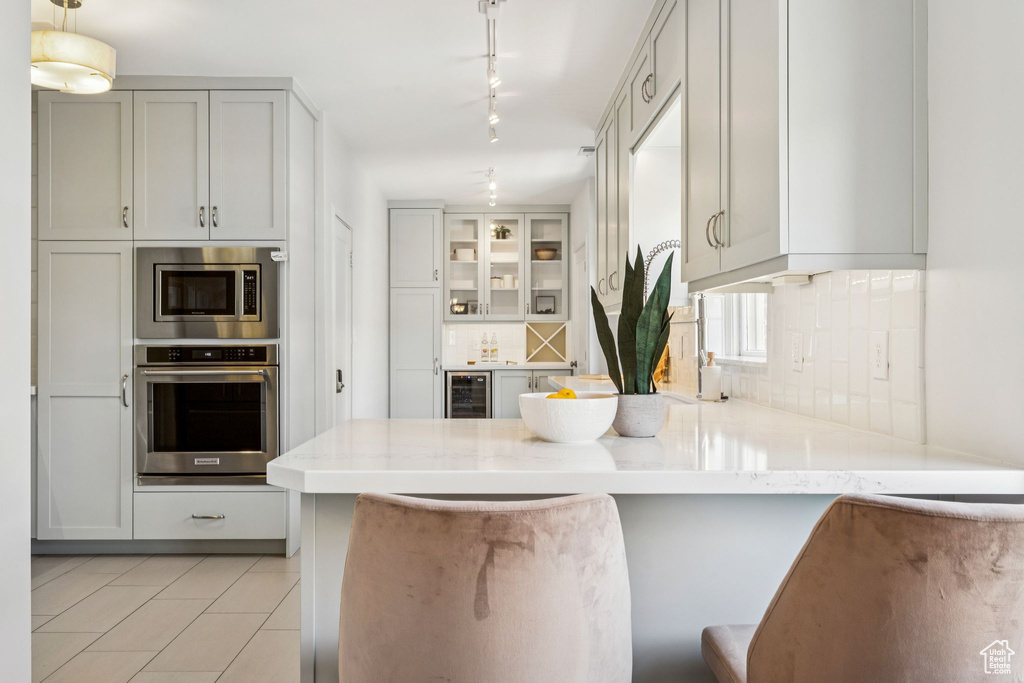 Kitchen featuring appliances with stainless steel finishes, wine cooler, a peninsula, backsplash, and light stone counters