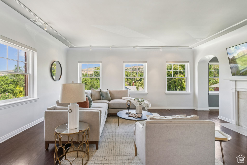 Living room with track lighting, dark wood-style floors, arched walkways, and healthy amount of natural light
