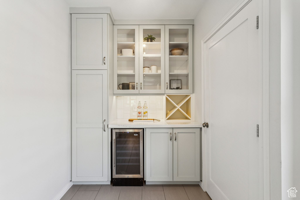 Indoor bar with wine cooler, light tile patterned floors, and decorative backsplash