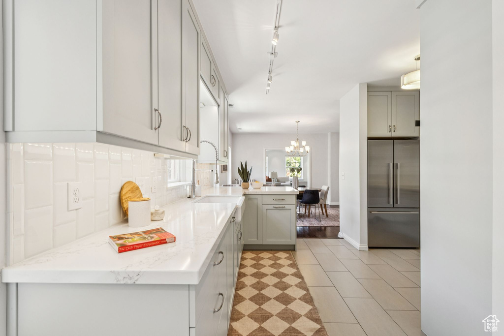 Kitchen featuring high end refrigerator, a peninsula, a chandelier, decorative backsplash, and gray cabinetry
