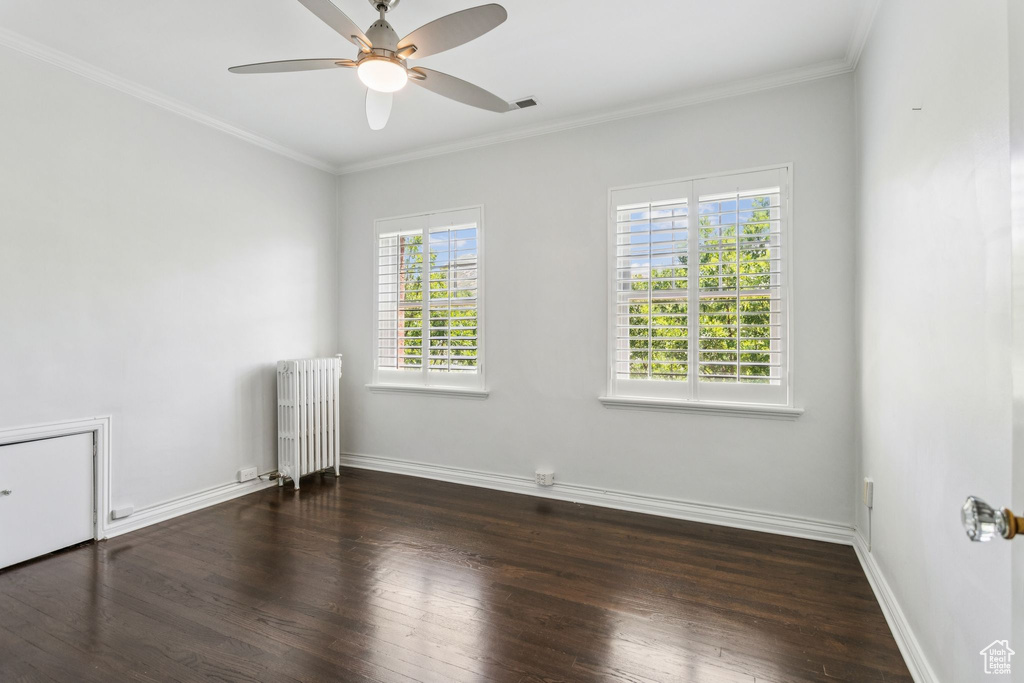 Unfurnished room featuring radiator, dark wood-style flooring, ceiling fan, and ornamental molding