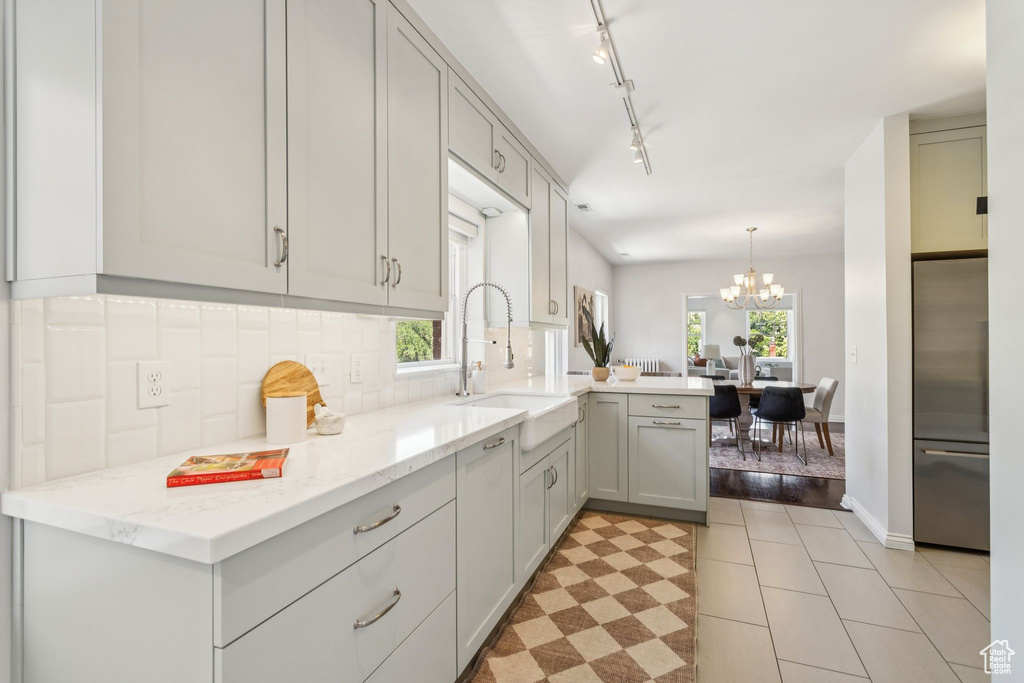 Kitchen featuring a peninsula, decorative backsplash, a chandelier, stainless steel refrigerator, and light stone counters