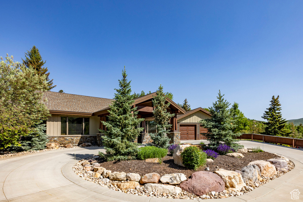 View of front of house featuring curved driveway, stone siding, and a shingled roof