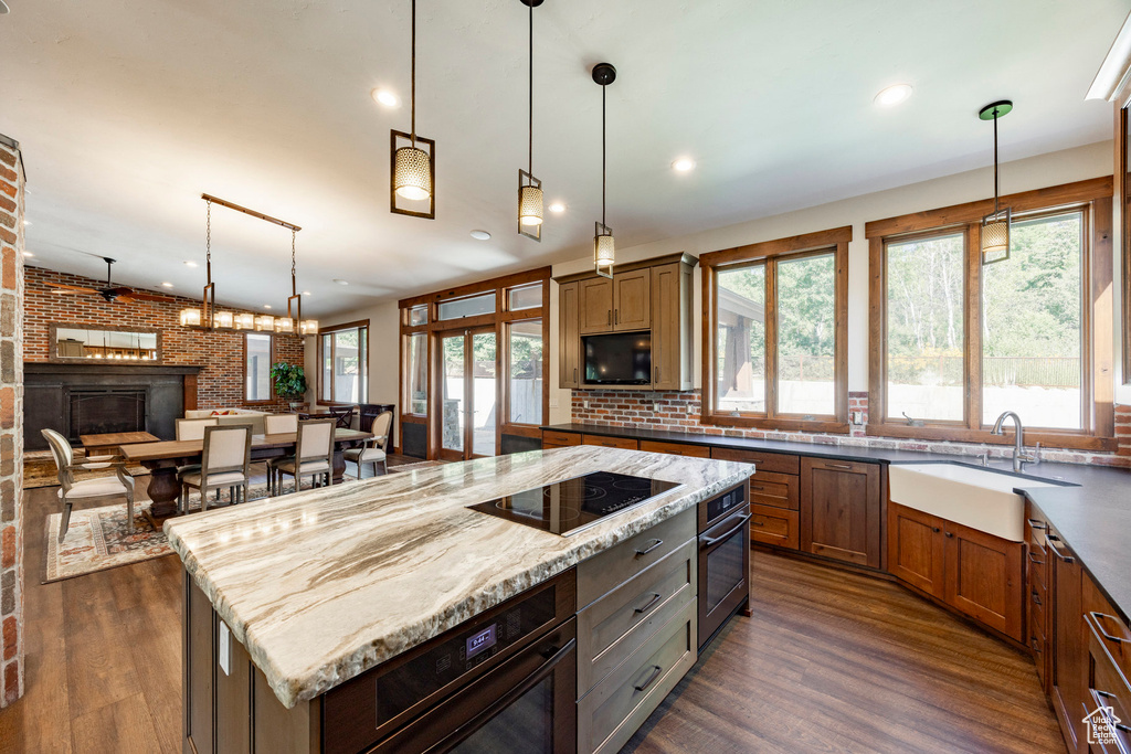 Kitchen with black electric cooktop, stainless steel oven, dark wood-style floors, light stone countertops, and recessed lighting