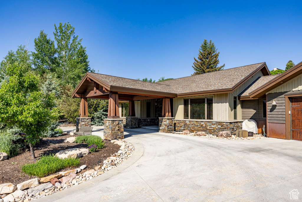 View of front of property with board and batten siding, roof with shingles, curved driveway, and stone siding