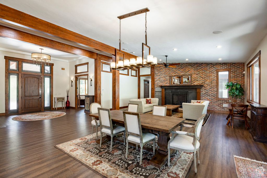 Dining space with brick wall, dark wood-style flooring, recessed lighting, a chandelier, and a fireplace