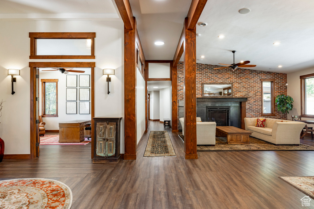 Living area featuring a ceiling fan, brick wall, wood finished floors, a glass covered fireplace, and recessed lighting