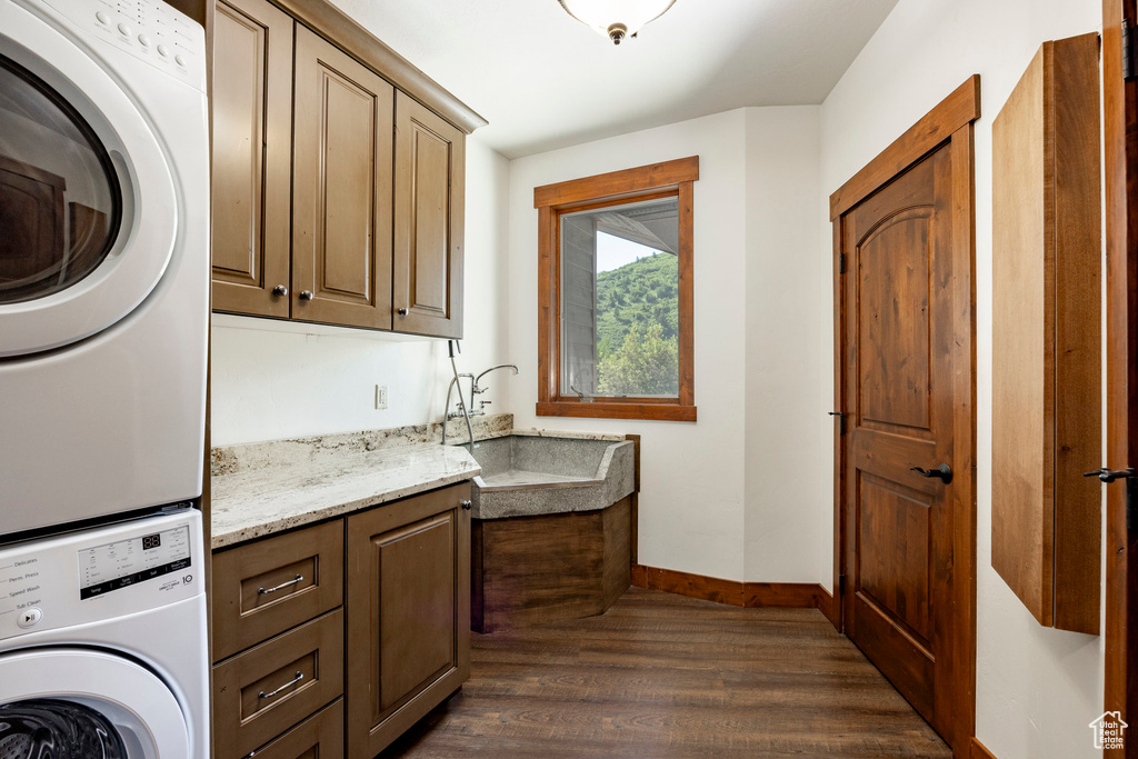 Laundry area with stacked washer / drying machine, cabinet space, and dark wood finished floors