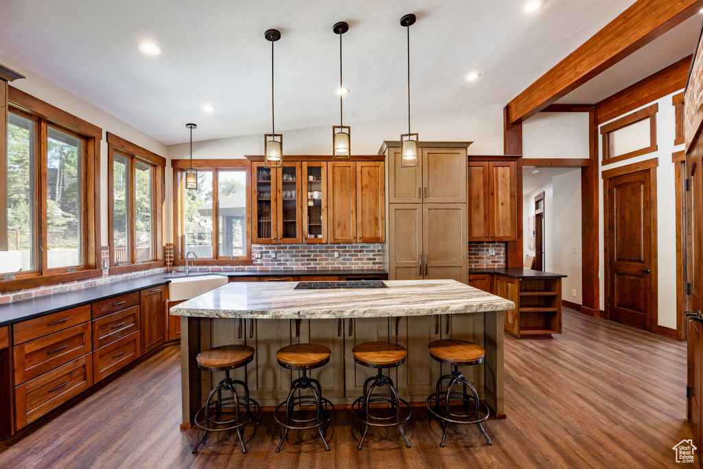 Kitchen featuring a kitchen island, decorative backsplash, dark wood finished floors, brown cabinets, and a breakfast bar