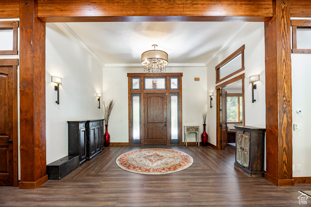 Foyer with a chandelier, crown molding, and dark wood-type flooring