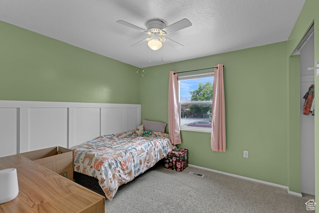 Carpeted bedroom featuring ceiling fan, a textured ceiling, and a wainscoted wall