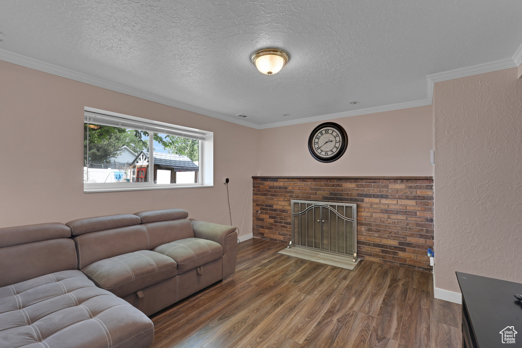 Living room with a textured ceiling, wood finished floors, a brick fireplace, and ornamental molding