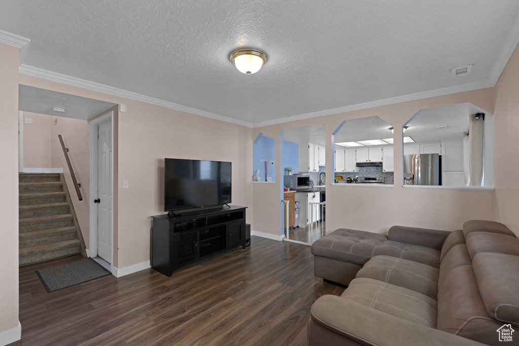 Living room featuring dark wood-style floors, crown molding, stairway, and a textured ceiling