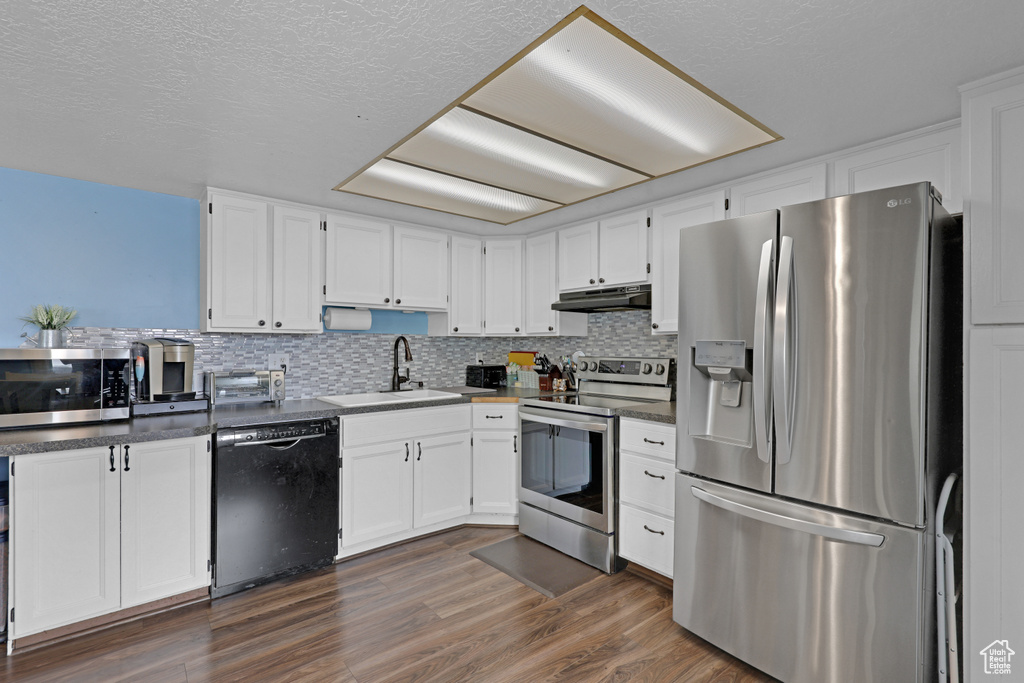 Kitchen featuring appliances with stainless steel finishes, under cabinet range hood, white cabinetry, tasteful backsplash, and a textured ceiling