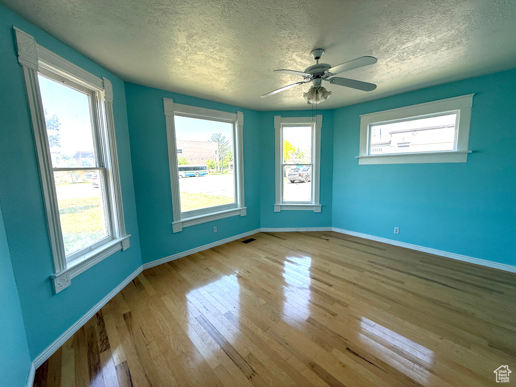 Unfurnished room with a textured ceiling, wood finished floors, plenty of natural light, and ceiling fan