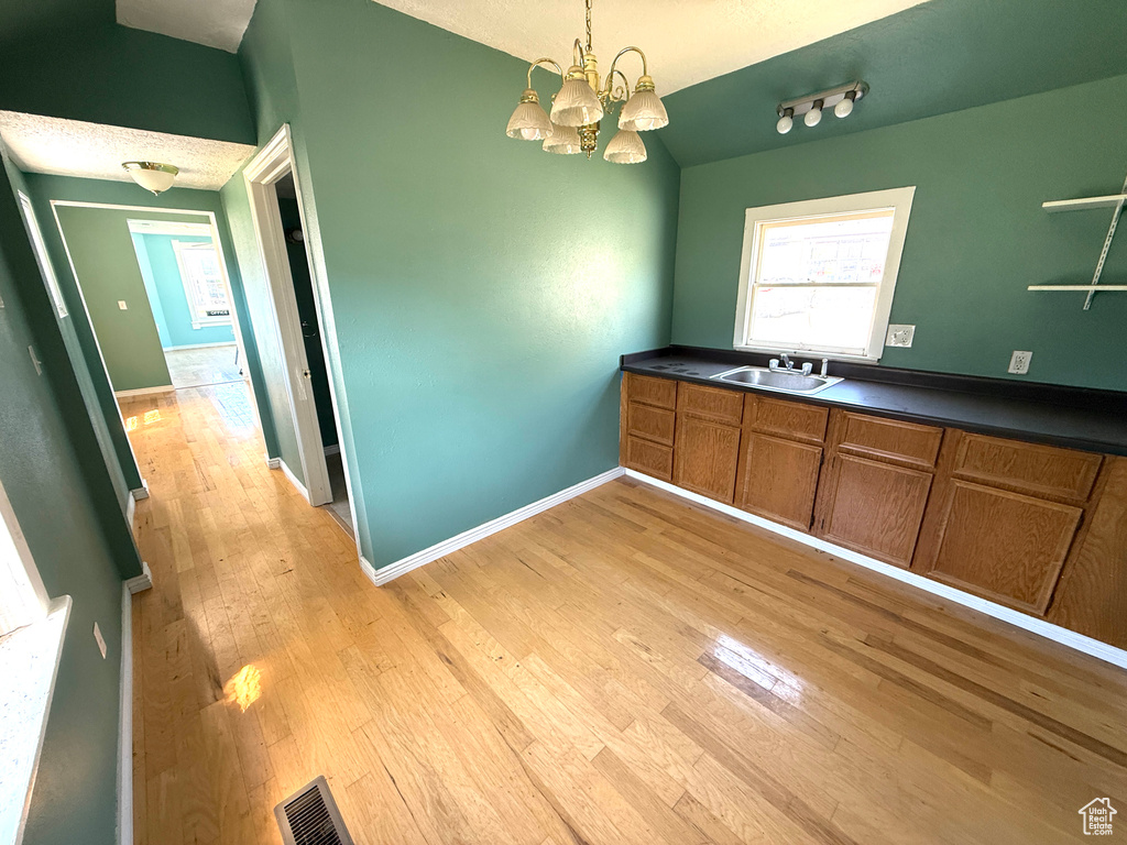 Kitchen with light wood-style flooring, brown cabinets, dark countertops, and a chandelier