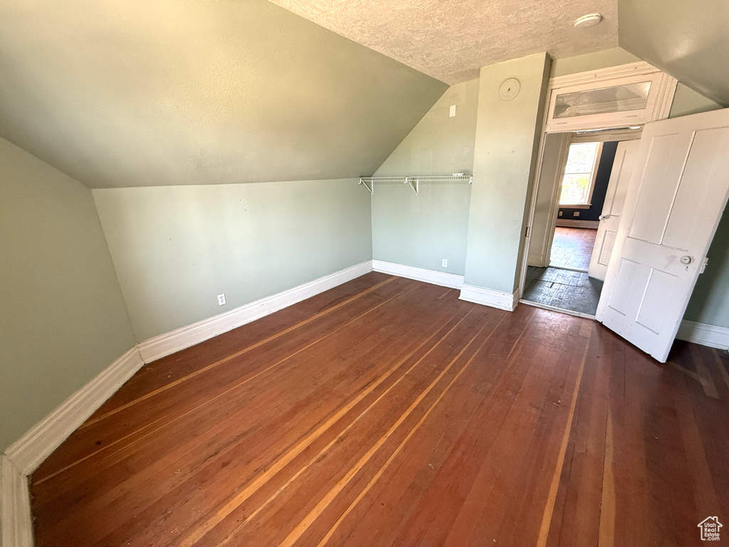 Additional living space featuring lofted ceiling, dark wood-type flooring, and a textured ceiling