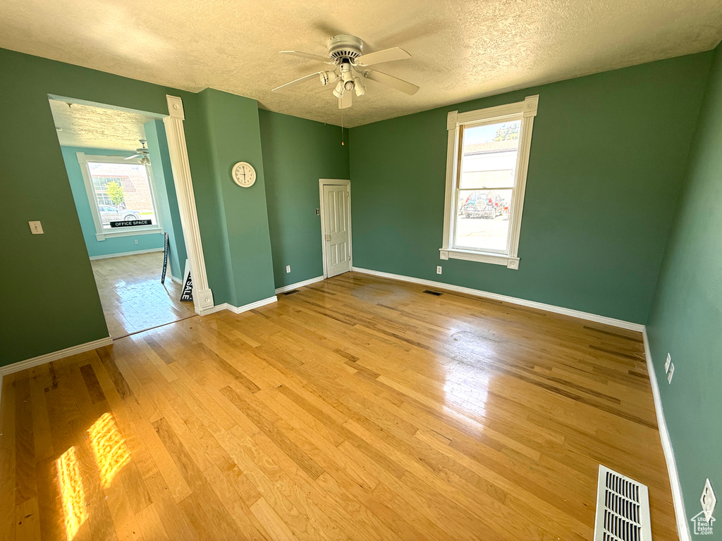 Empty room with ceiling fan, a textured ceiling, and wood finished floors