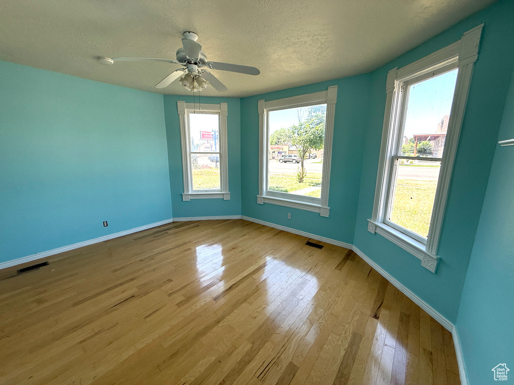 Spare room featuring wood finished floors, a textured ceiling, healthy amount of natural light, and a ceiling fan