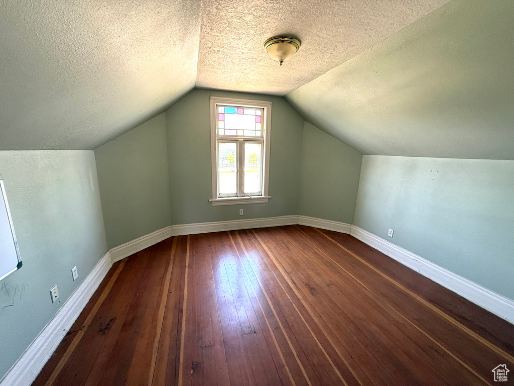 Additional living space with dark wood-style floors, a textured ceiling, and lofted ceiling