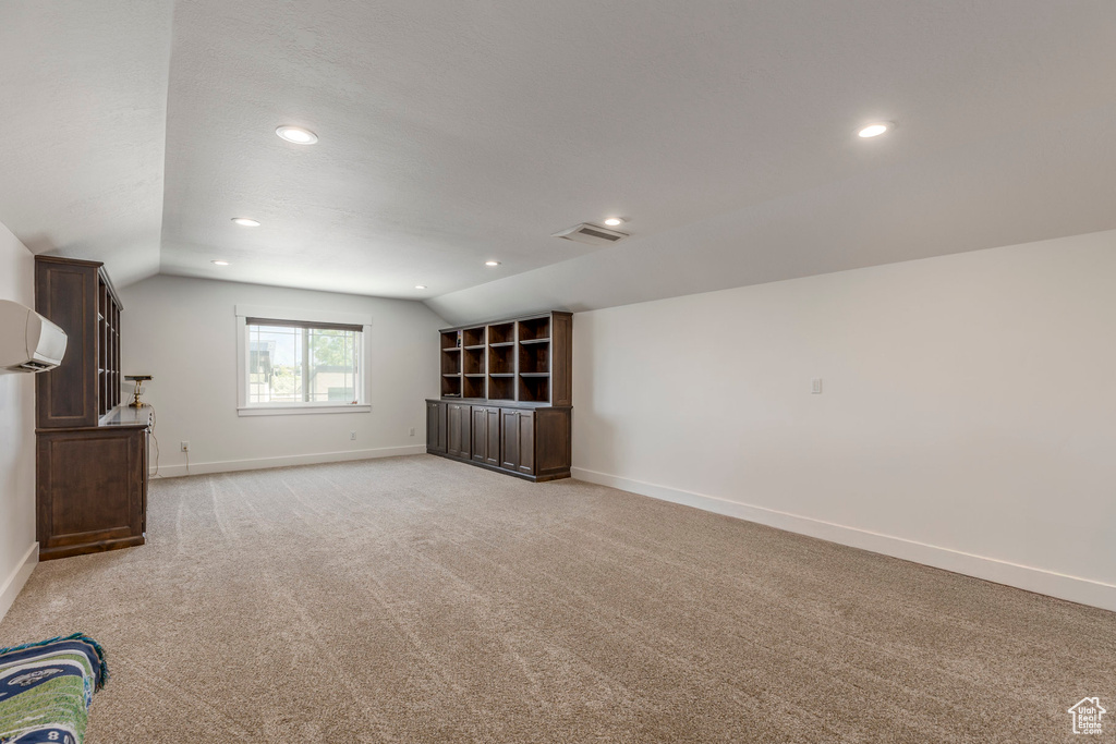 Unfurnished living room with lofted ceiling, light colored carpet, recessed lighting, and a wall unit AC