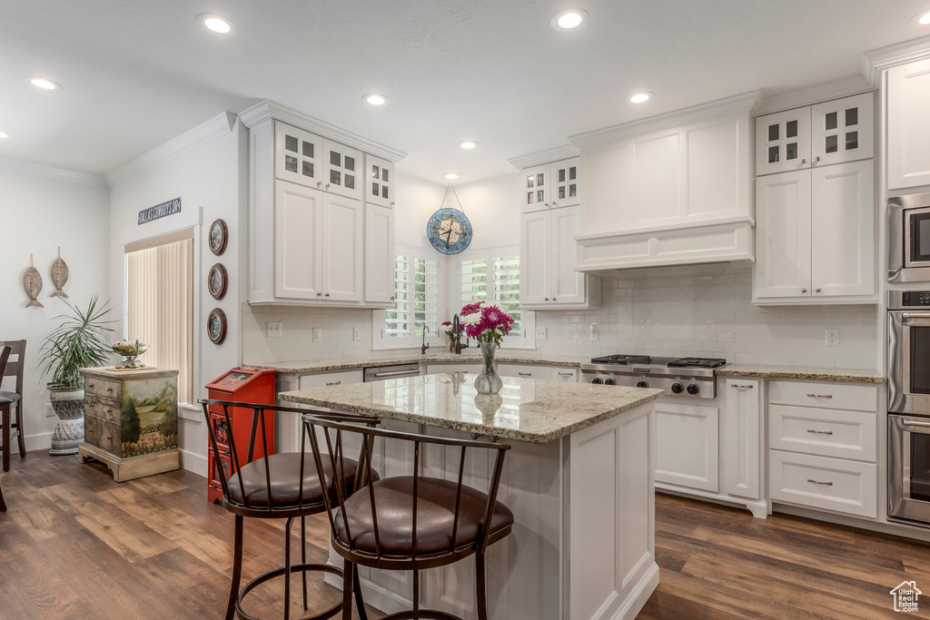 Kitchen with stainless steel gas stovetop, white cabinets, a kitchen bar, crown molding, and recessed lighting