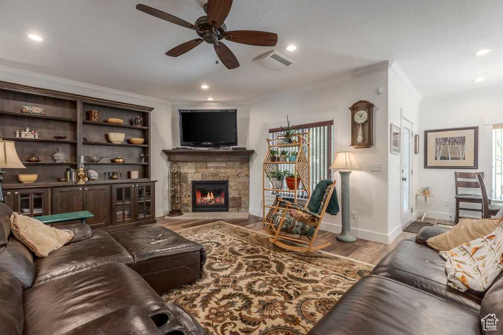 Living area featuring ornamental molding, a fireplace, ceiling fan, wood finished floors, and recessed lighting
