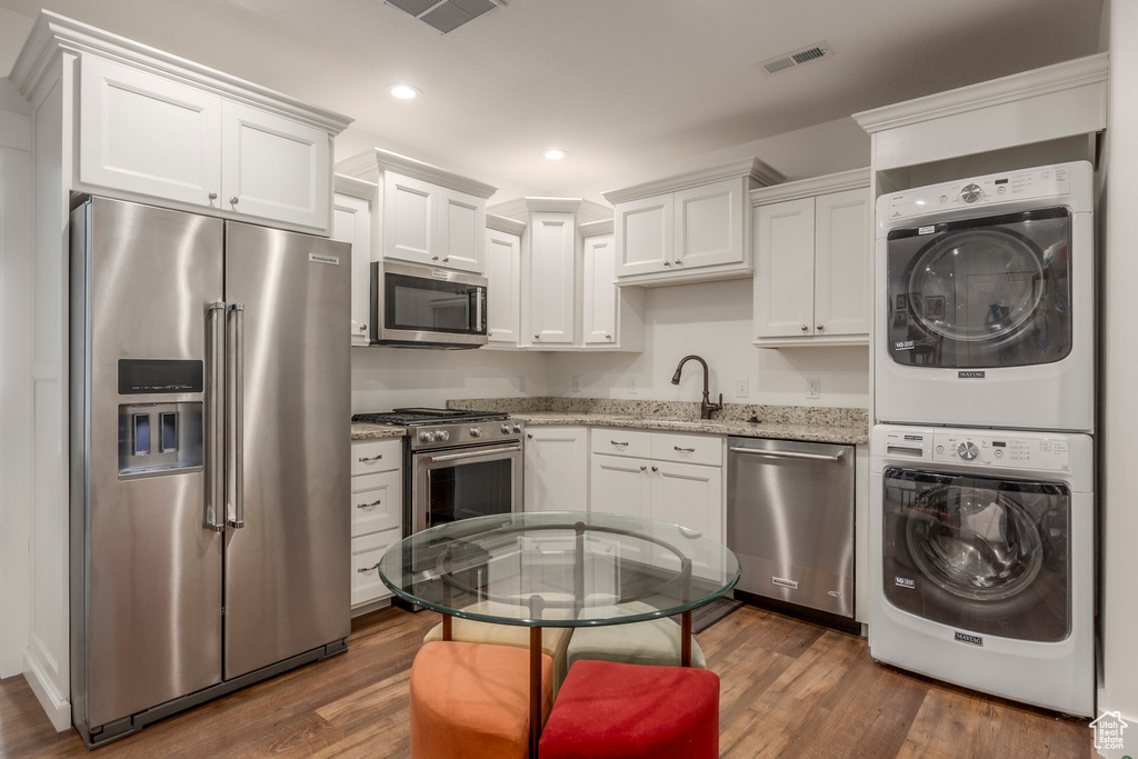Kitchen featuring stainless steel appliances, estacked washer and dryer, light stone counters, dark wood finished floors, and recessed lighting