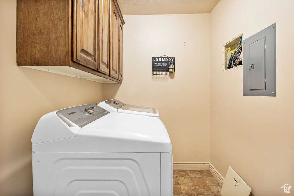 Laundry room featuring electric panel, washing machine and clothes dryer, cabinet space, and stone finish floors