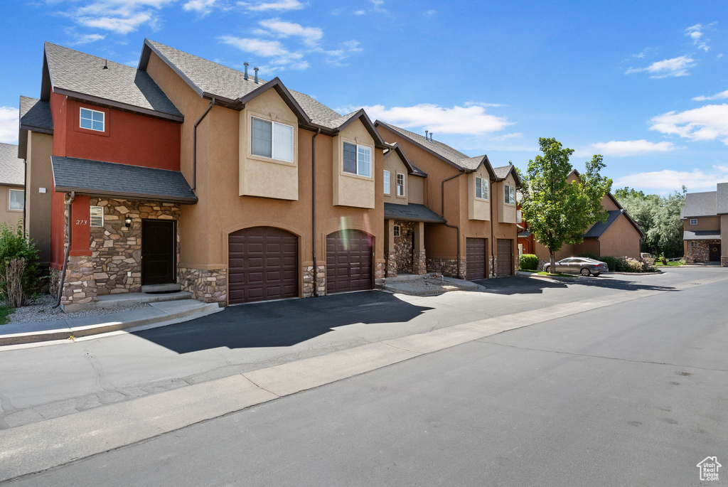Townhome / multi-family property with stone siding, a residential view, an attached garage, stucco siding, and driveway