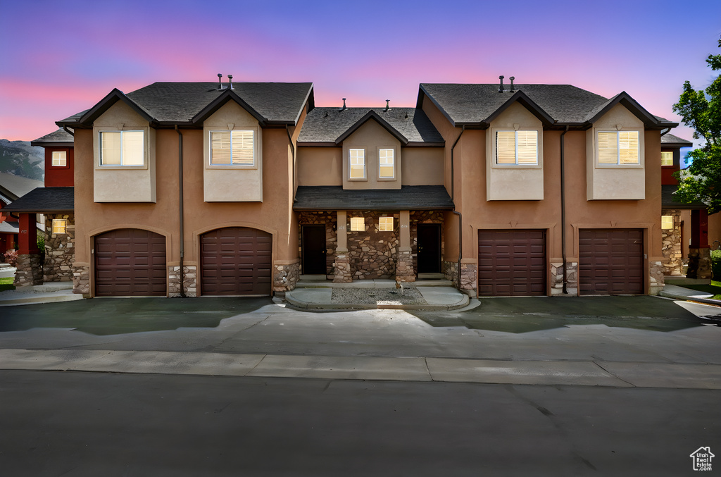 Townhome / multi-family property with an attached garage, stucco siding, and stone siding