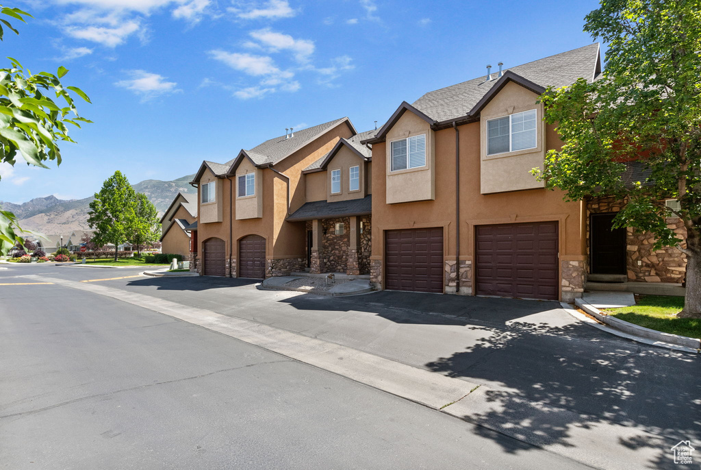 View of property featuring stone siding, stucco siding, a garage, a mountain view, and a residential view