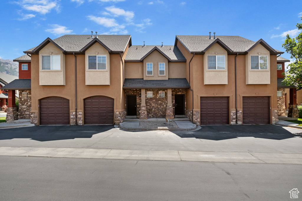 View of property featuring a garage, stone siding, and stucco siding