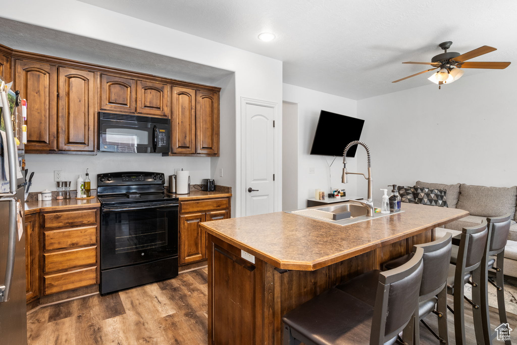 Kitchen featuring black appliances, ceiling fan, a breakfast bar area, and dark wood finished floors