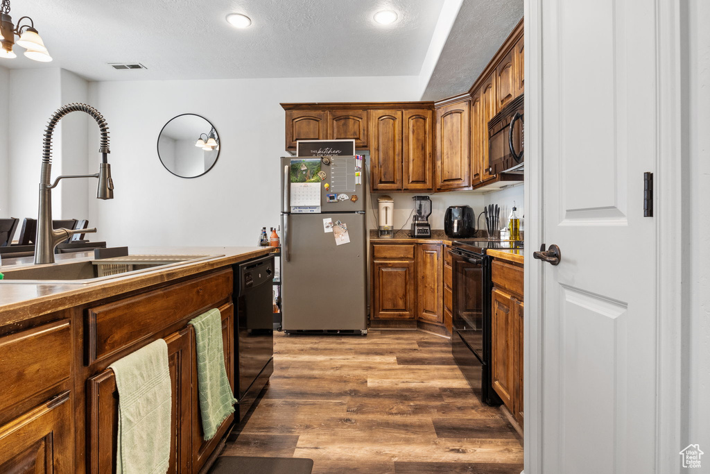 Kitchen featuring black appliances, wood finished floors, recessed lighting, brown cabinets, and a textured ceiling