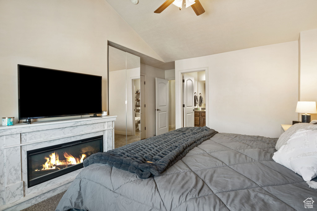 Carpeted bedroom with vaulted ceiling, a fireplace, ceiling fan, and ensuite bathroom