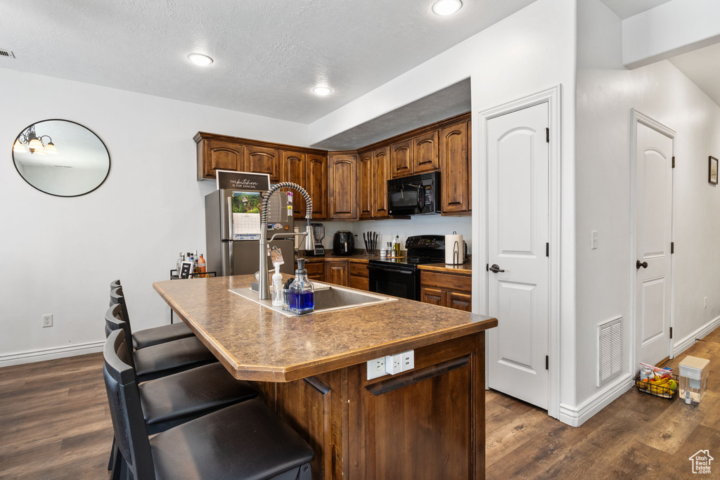 Kitchen featuring black appliances, dark wood-style flooring, an island with sink, recessed lighting, and a breakfast bar area