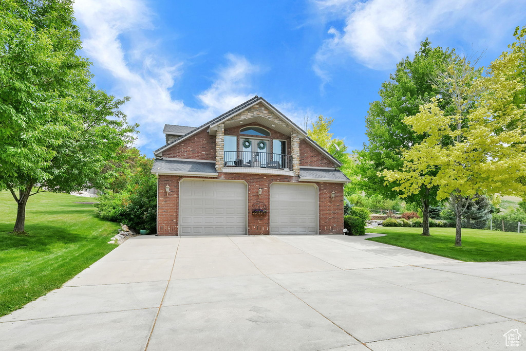 Traditional home featuring an attached garage, brick siding, concrete driveway, a balcony, and a front yard