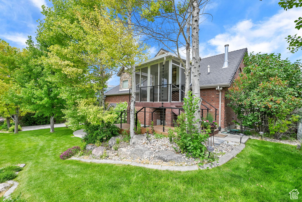 Back of property with a sunroom, brick siding, a yard, and roof with shingles