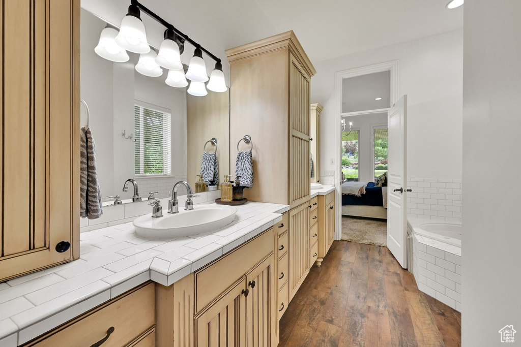 Ensuite bathroom with vanity, wood finished floors, a relaxing tiled tub, and recessed lighting
