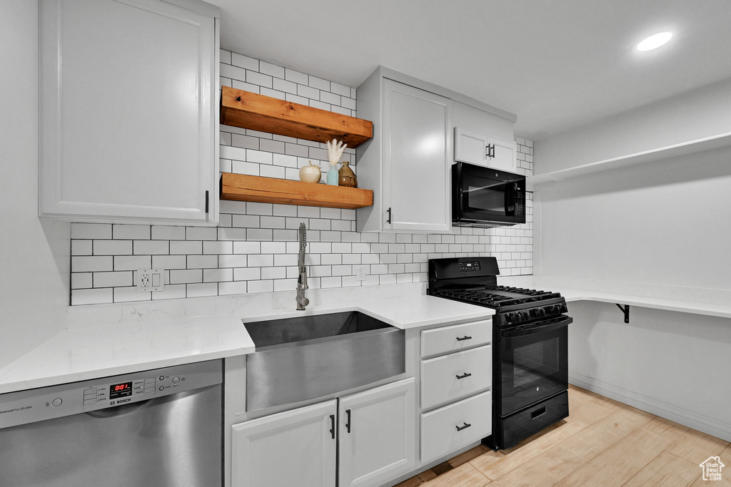 Kitchen with black appliances, open shelves, light wood-style flooring, tasteful backsplash, and light countertops