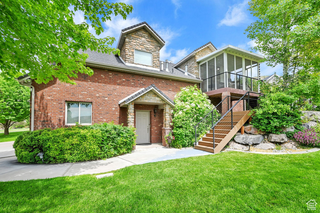 View of front of property with a sunroom, a front yard, stairs, brick siding, and stone siding