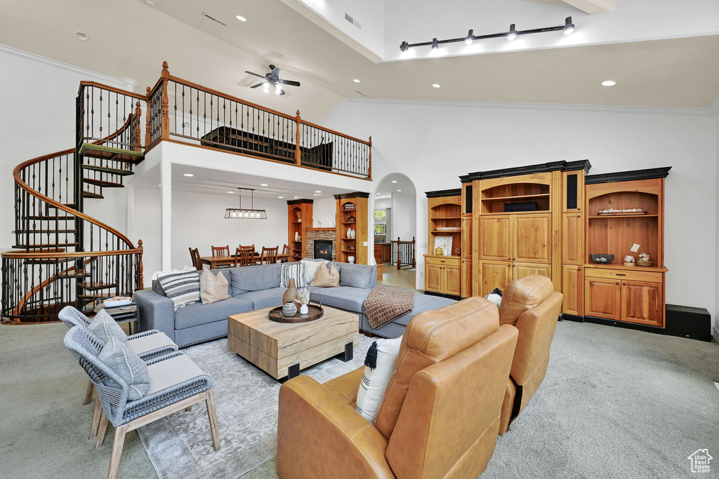 Living area with light carpet, stairs, arched walkways, a ceiling fan, and high vaulted ceiling