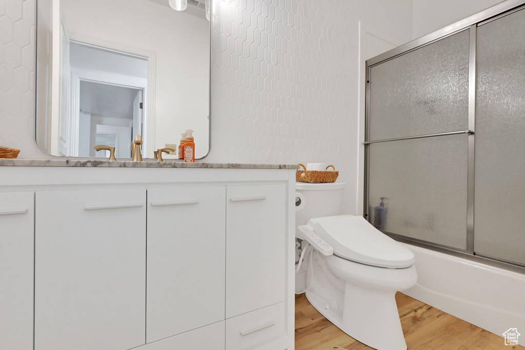 Full bathroom with wood finished floors, vanity, and combined bath / shower with glass door