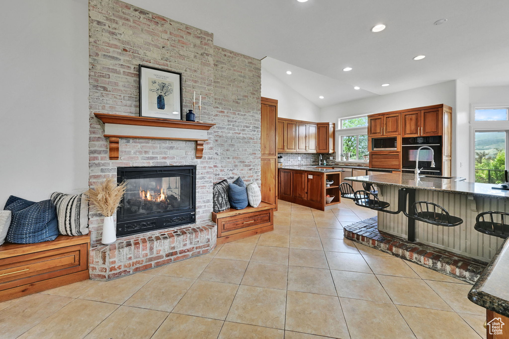 Kitchen with vaulted ceiling, light tile patterned flooring, black appliances, recessed lighting, and a kitchen bar
