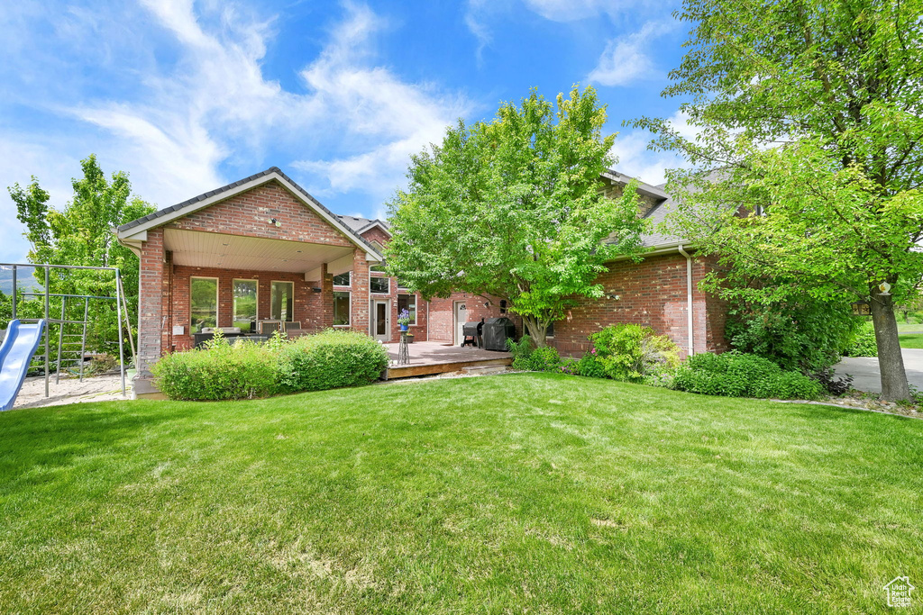 Rear view of property with brick siding, a lawn, and a deck