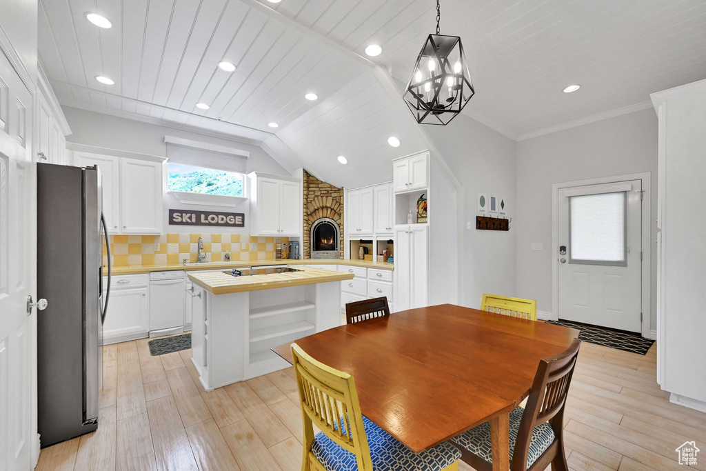 Dining space featuring light wood-style flooring, a stone fireplace, a chandelier, recessed lighting, and vaulted ceiling