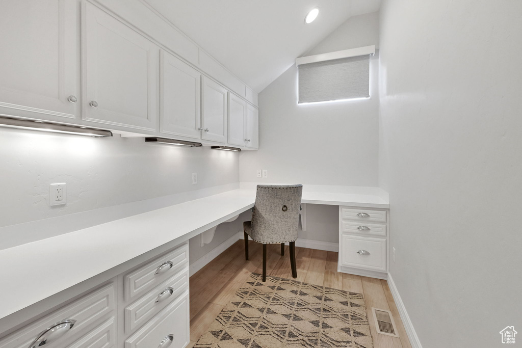 Unfurnished office with built in desk, lofted ceiling, and light wood-style floors