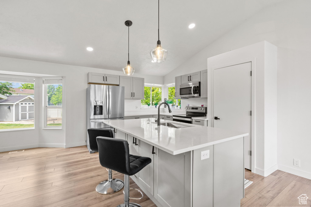 Kitchen featuring appliances with stainless steel finishes, gray cabinetry, light countertops, a kitchen bar, and vaulted ceiling